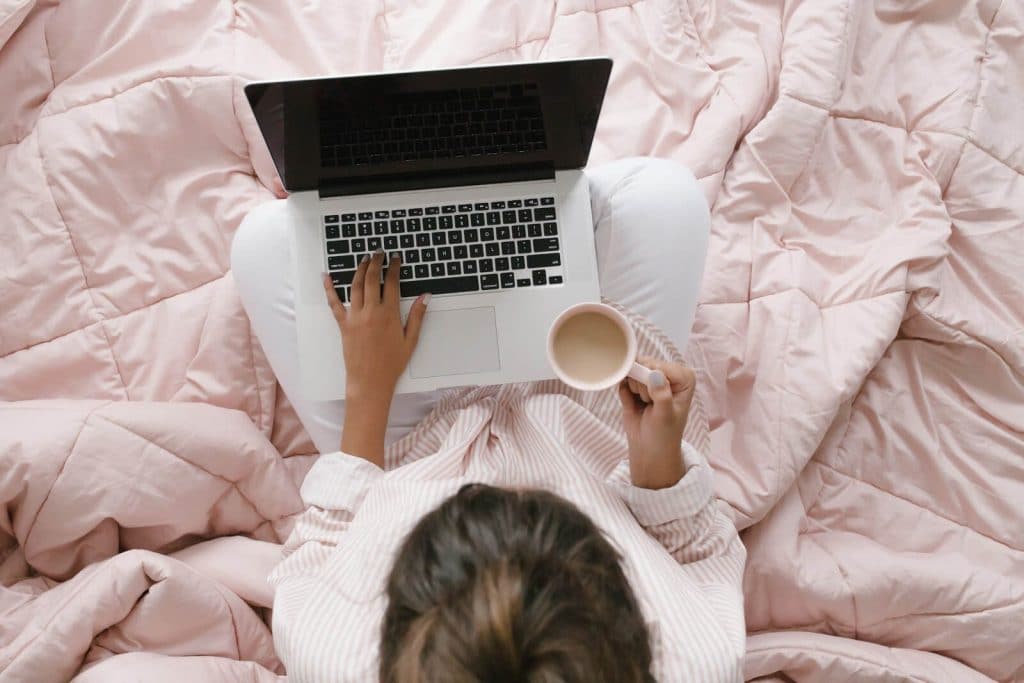 Woman working on a laptop and sitting on a bed