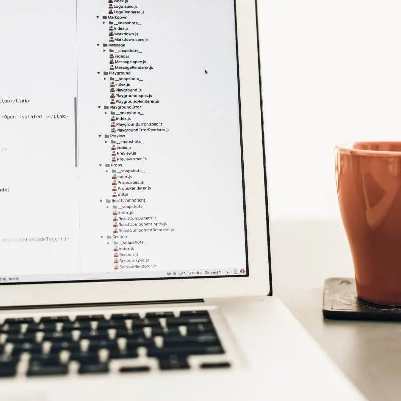 A laptop showing code and a mug next to it