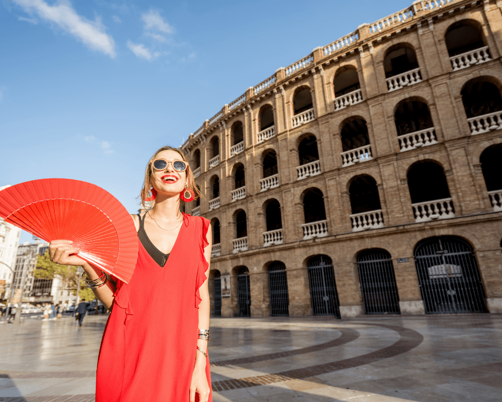 A woman in red dress with a fan in front of the bullring in Valencia