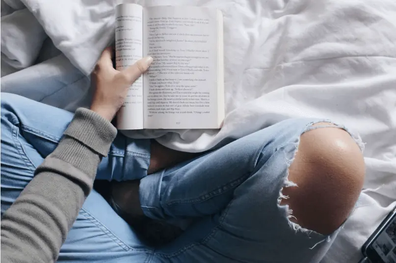 girl reading book on bed
