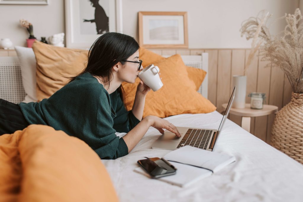 girl working from bed drinking coffee